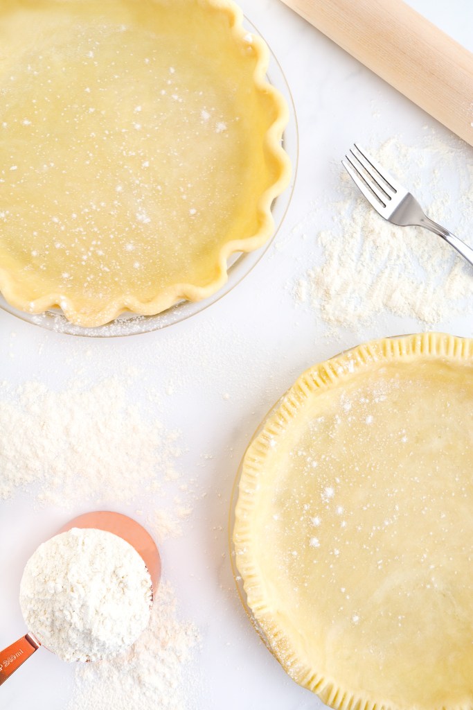 Two pie crusts and sprinkled flour on marble countertop