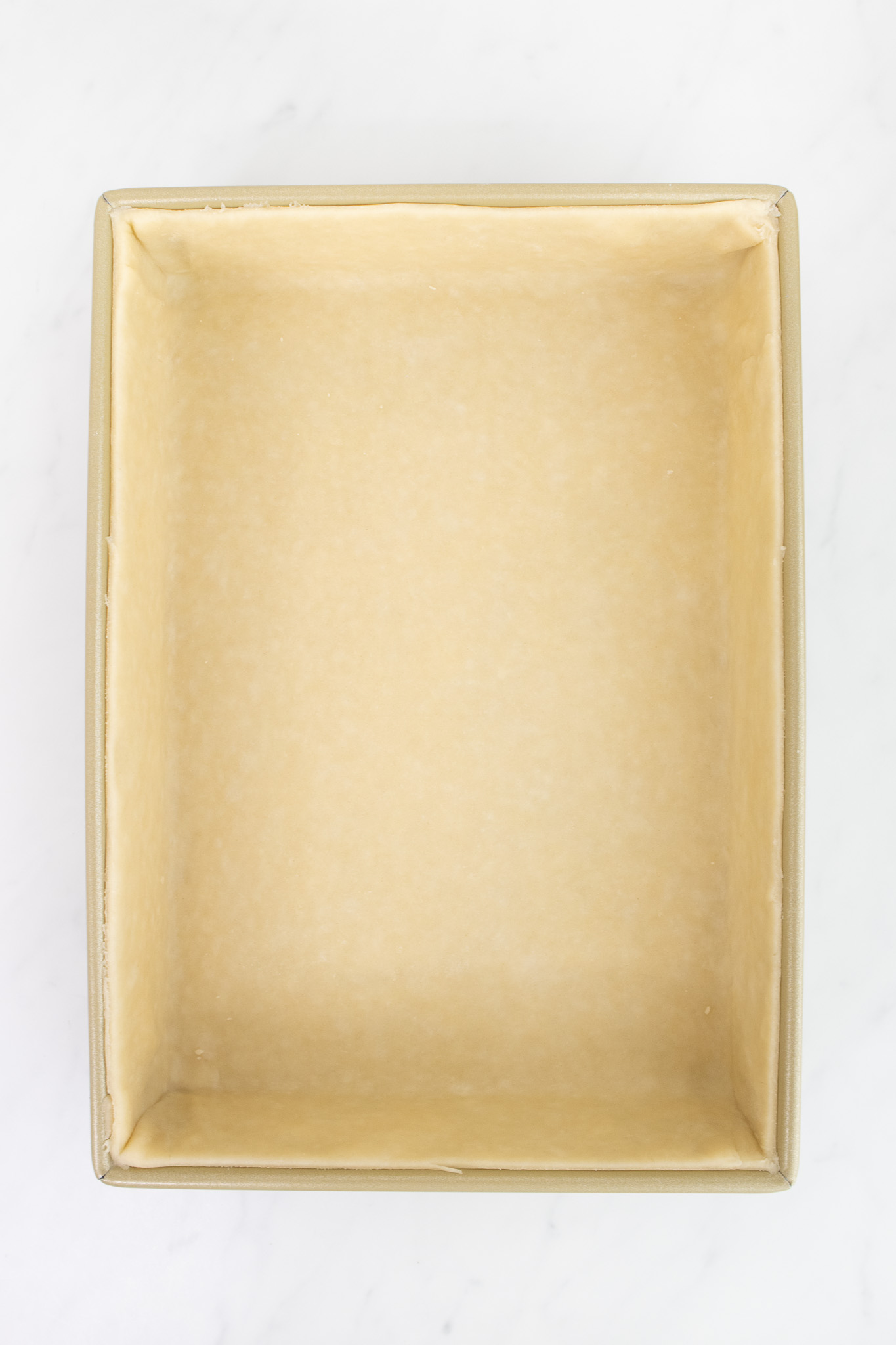 A rectangular baking pan lined with an unbaked pastry crust, set on a white marble surface.