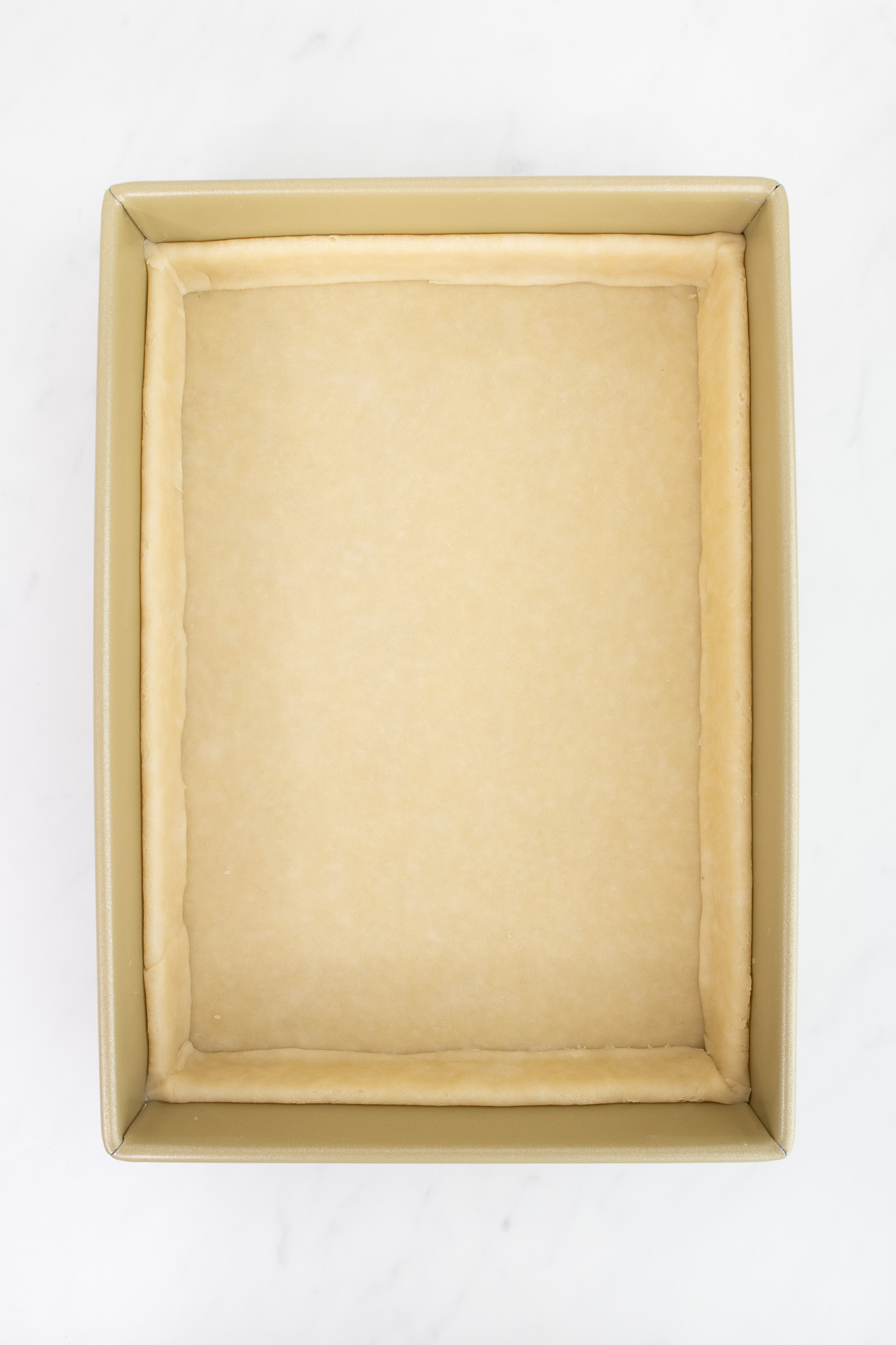 A 9 by 13 inch baking pan with raw pastry dough pressed into the bottom and sides.