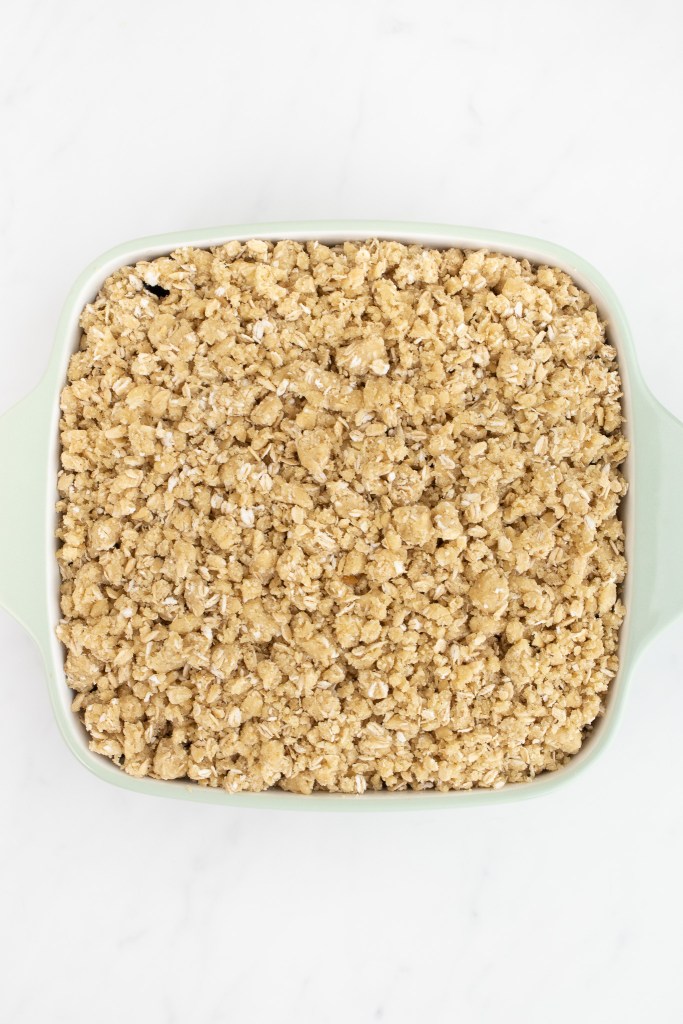 Square baking dish filled with unbaked blueberry crisp on a white marble surface.