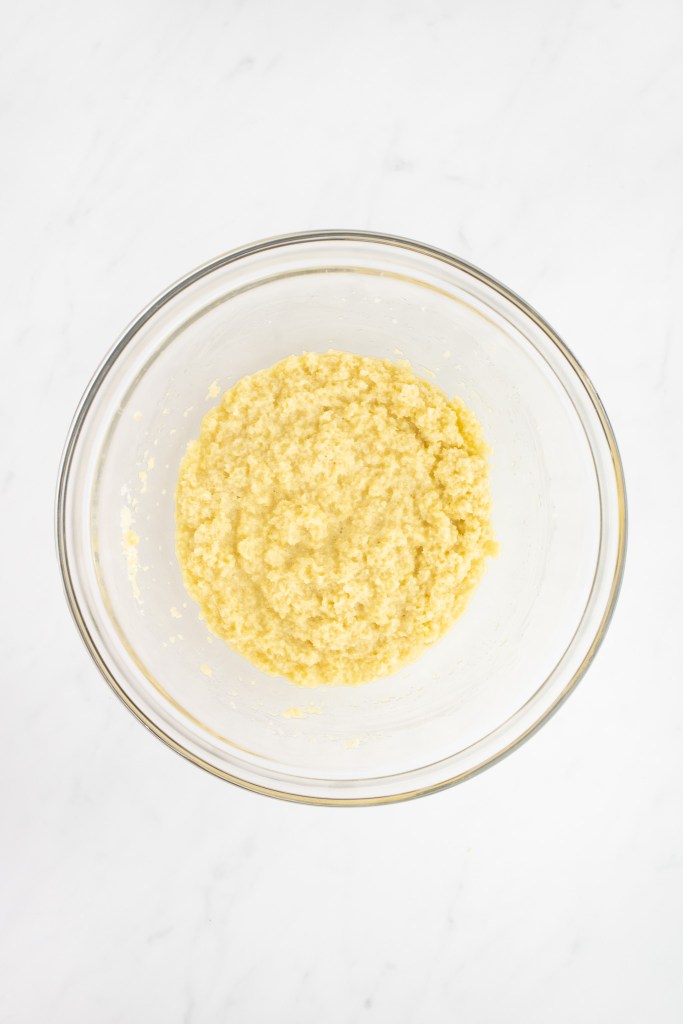 A clear glass bowl filled with milk, panko and egg mixture sits on a white marble surface.