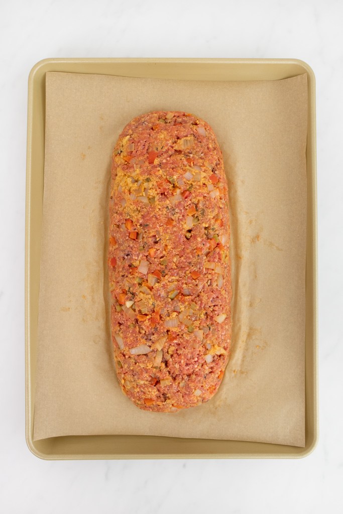 Uncooked meatloaf mixture shaped into a loaf on a parchment-lined baking sheet, ready to be baked.