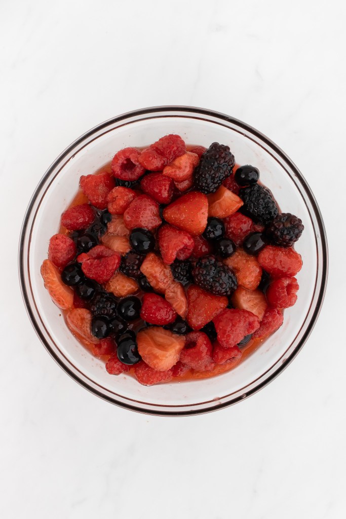 A glass bowl containing finished mixed berry cheesecake topping on a white marble surface