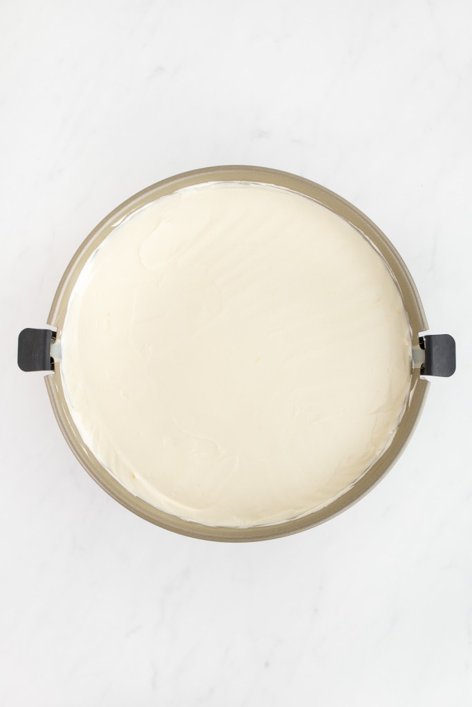 A springform pan filled with cream cheese filling sits on a white marble surface.