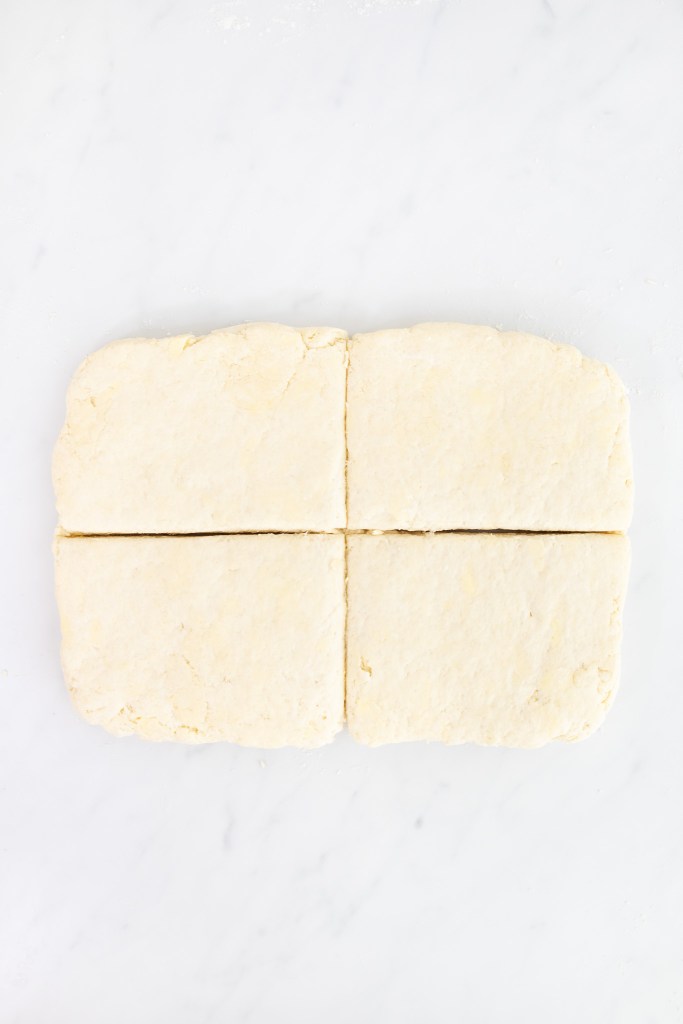 Rectangular strawberry shortcake dough, rolled out and cut into four equal pieces, rests on a white marble surface.