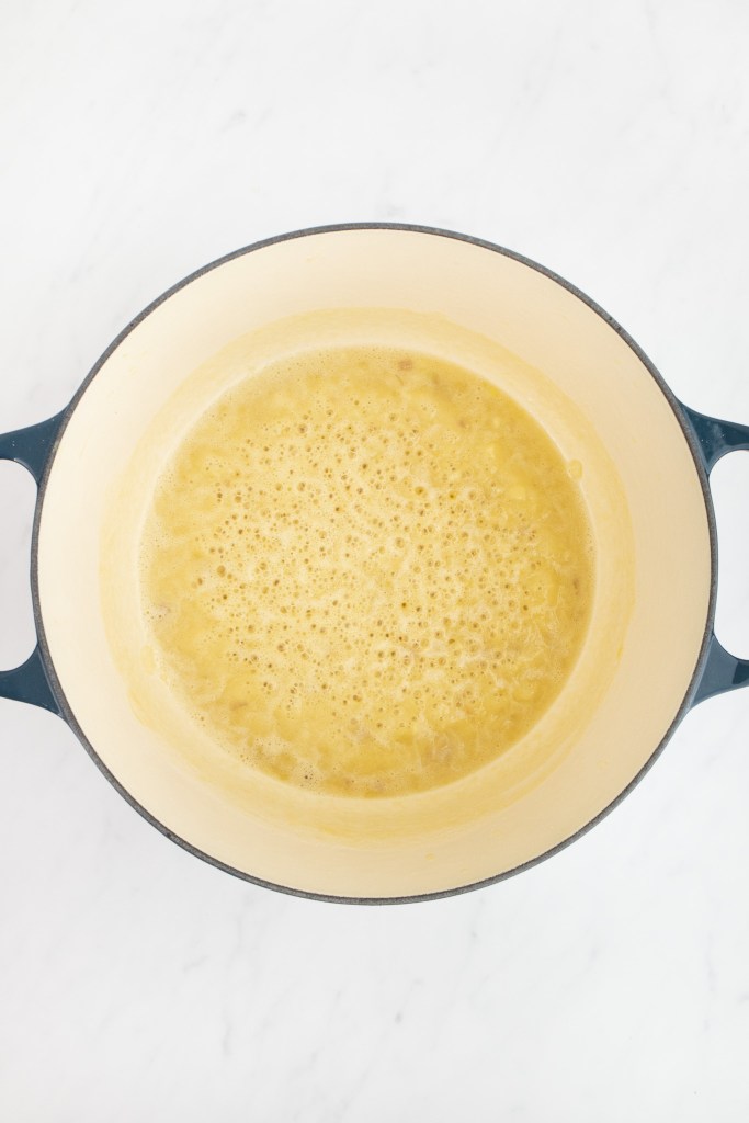 A dutch oven containing a bubbling roux mixture sits on a white marble surface.