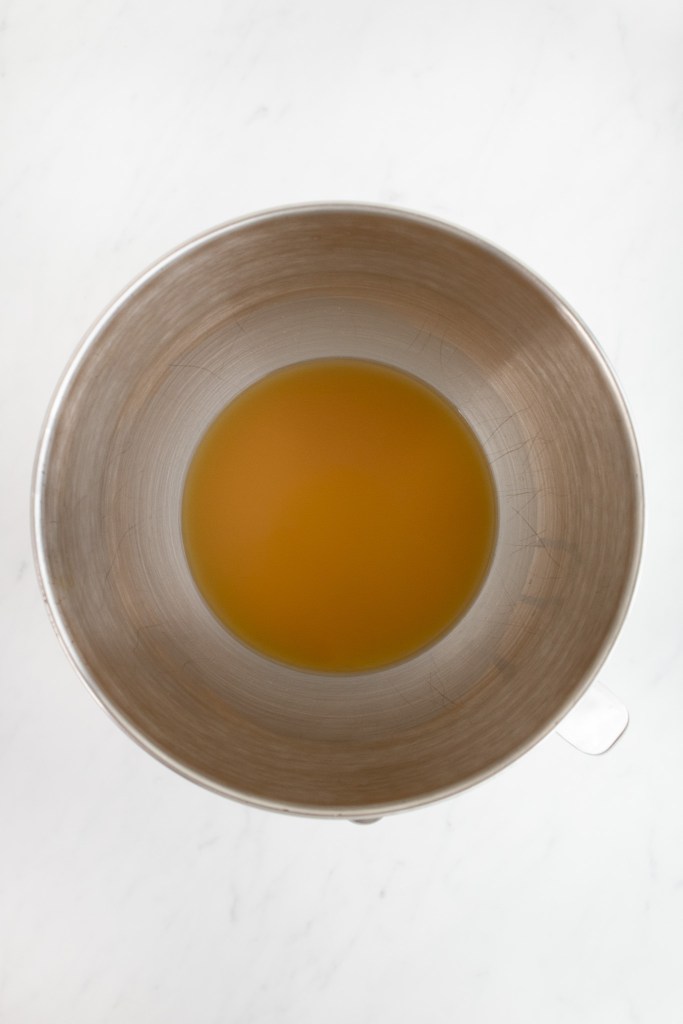 The bowl of an electric stand mixer containing yeast mixture.