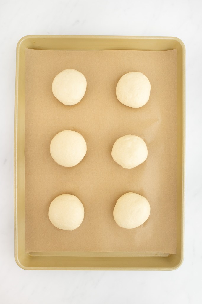 Six balls of bagel dough arranged in two columns on a parchment-lined baking sheet.
